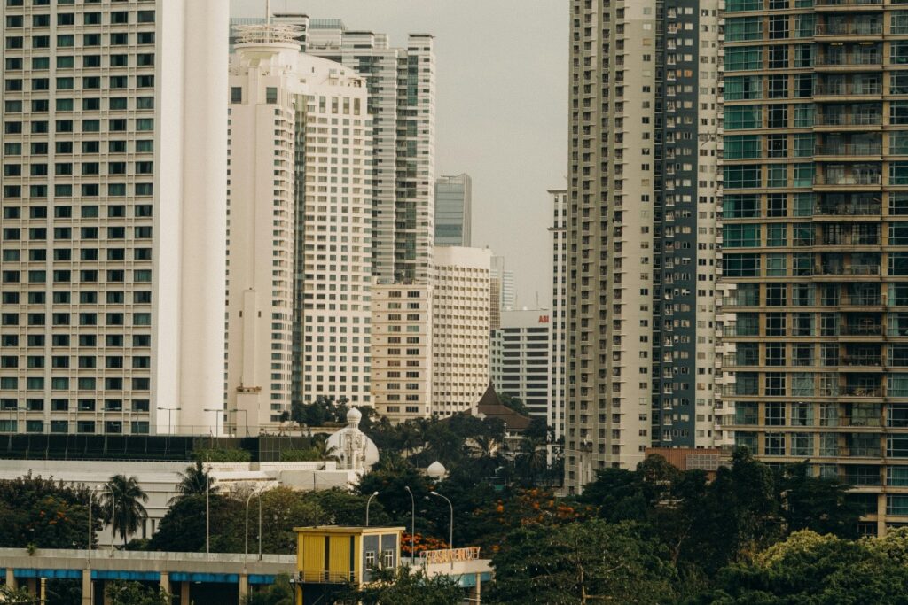 Gambar ini menampilkan pemandangan urbana dengan sejumlah gedung - gedung tinggi yang beragam bentuk dan desain. Ada gedung - gedung modern dengan bangunan kaca dan baja, serta beberapa bangunan yang memiliki elemen - elemen khas seperti kubah putih. Di antara gedung - gedung tersebut, juga terlihat pohon - pohon yang memberikan sentuhan hijau. Sama seperti bagaimana gedung - gedung ini membentuk komunitas perkotaan yang padat dan bervariasi, Shopee Live Indonesia menawarkan keuntungan bagi para penjual. Mereka dapat mencapai audiens yang lebih luas, menunjukkan produk secara langsung, dan berinteraksi dengan pelanggan, membentuk sebuah komunitas jualan yang dinamis dan efektif.