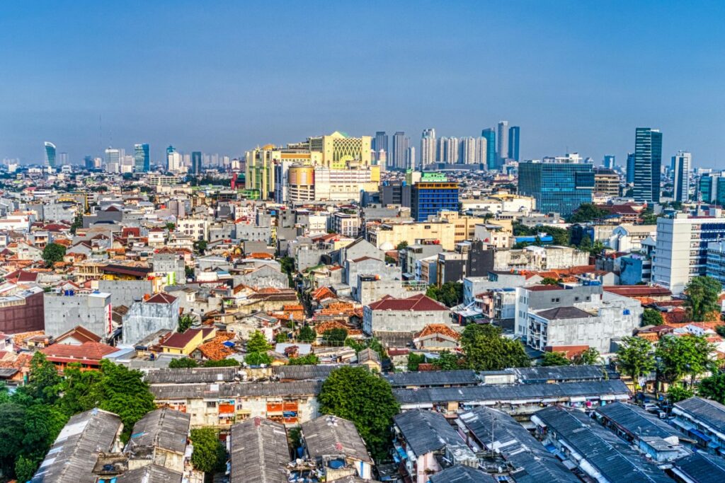 Tampilan overhead dari kota yang menggabungkan kawasan perkotaan modern dengan bangunan - bangunan tinggi di latar belakang dan perkampungan dengan atap - atap tua di depan. Pemasaran Media Sosial di Indonesia Apa yang Berubah di 2025
