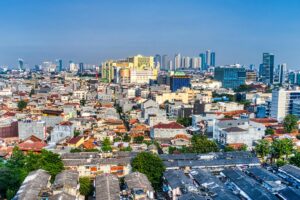 Tampilan overhead dari kota yang menggabungkan kawasan perkotaan modern dengan bangunan - bangunan tinggi di latar belakang dan perkampungan dengan atap - atap tua di depan. Pemasaran Media Sosial di Indonesia Apa yang Berubah di 2025