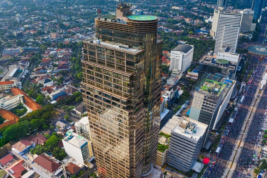 Gambar ini memaparkan pemandangan dari atas sebuah kota yang padat dengan gedung - gedung. Di tengahnya, ada gedung tingginya yang mencolok dengan lapisan kaca yang memantulkan cahaya. Di sekitarnya, berbagai tipe bangunan mulai dari rumah - rumah dengan atap merah sampai gedung - gedung modern, dan jalanan yang padat dengan orang dan kendaraan. Sama seperti kota yang penuh dengan potensi menarik untuk diangkat ke layar, di TikTok Indonesia, bisnis dapat menggunakan berbagai tips untuk membuat video viral. Misalnya, memanfaatkan tren lokal, menampilkan sisi unik dari produk atau layanan, serta menggunakan musik dan efek yang tepat, semua ini seperti elemen - elemen di dalam kota yang membuatnya menarik dan dapat menarik perhatian banyak orang.